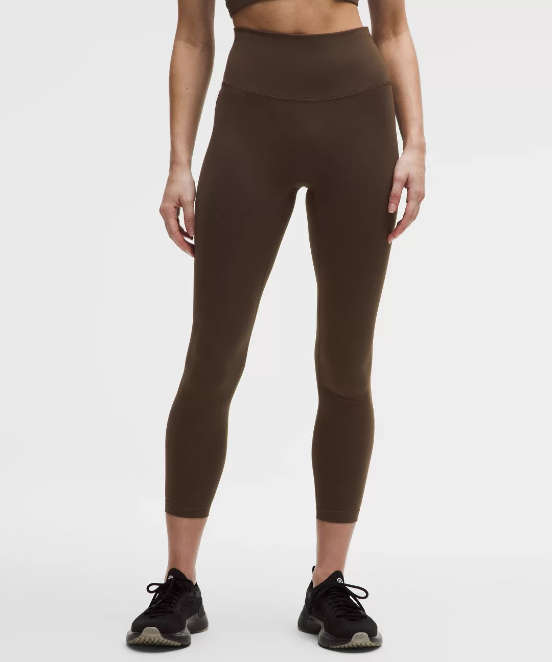 Person wearing brown high-waisted leggings on a white background