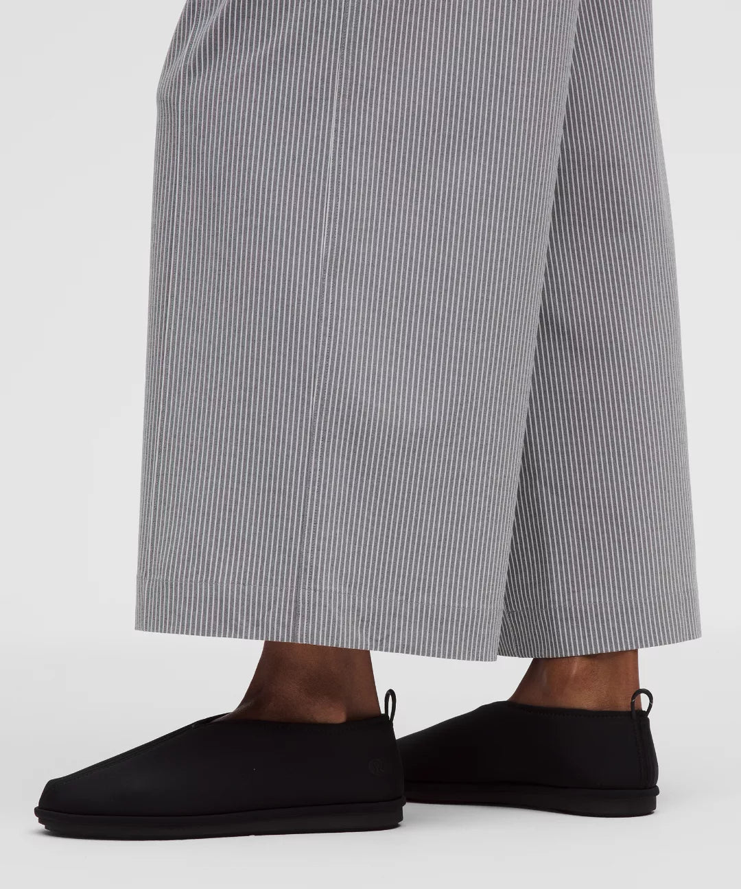 Person wearing black slip-on shoes and gray striped pants on a white background
