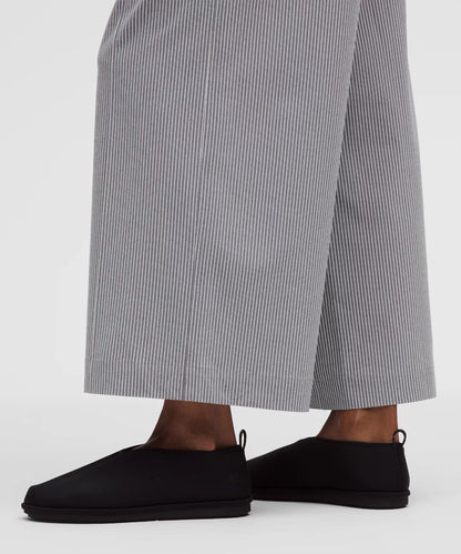 Person wearing black slip-on shoes and gray striped pants on a white background