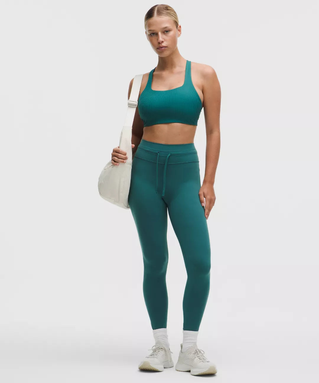 Woman wearing a green athletic outfit holding a white bag on a light gray background
