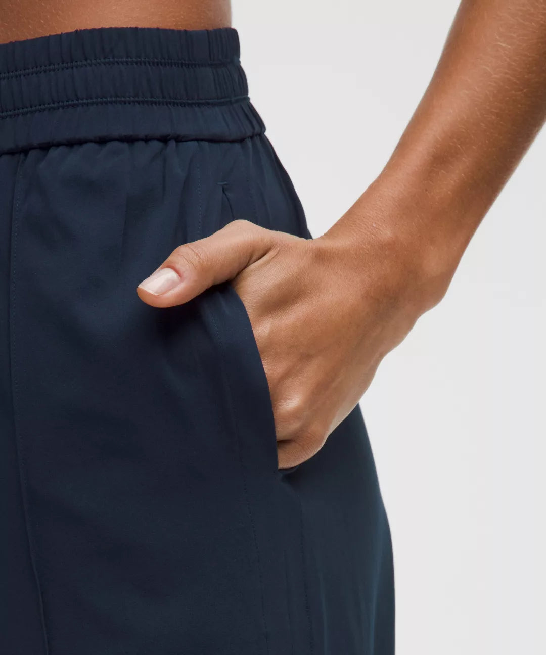 Navy blue pants with a hand adjusting the waistband against a light background