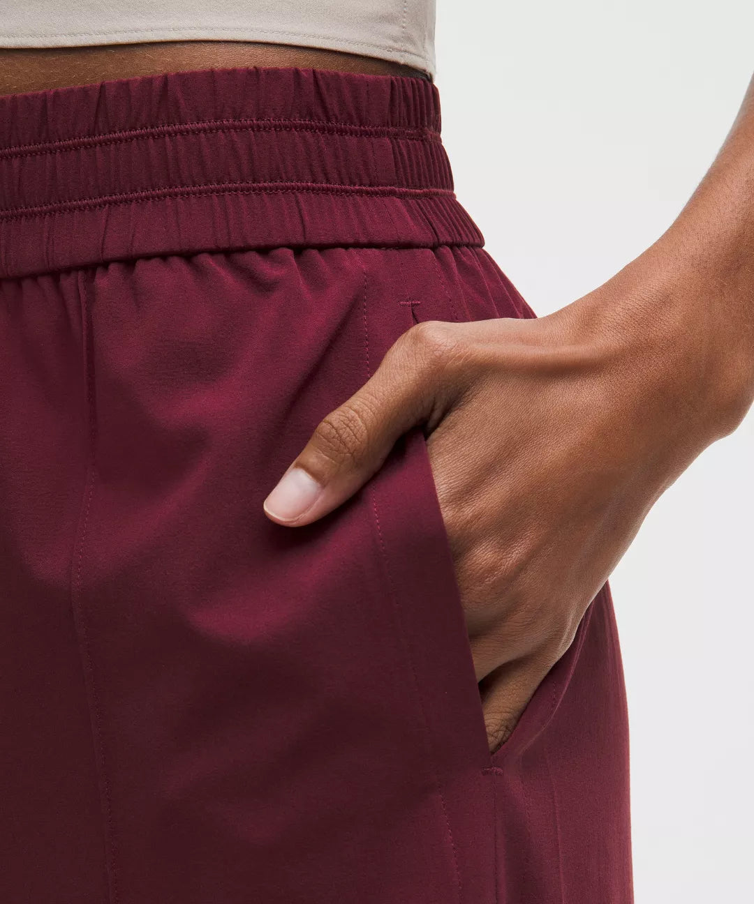 Maroon pants with a hand adjusting the waistband on a plain background