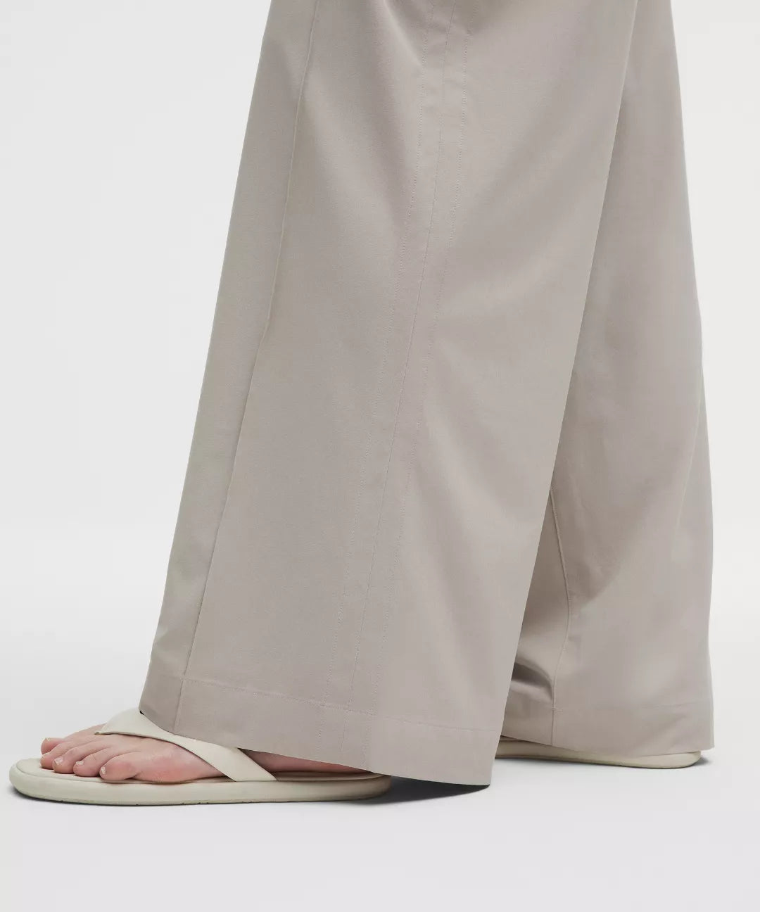 Person wearing beige wide-leg pants and white sandals on a light gray background