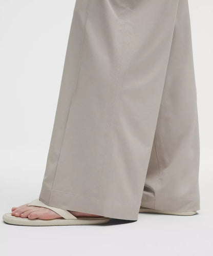 Person wearing beige wide-leg pants and white sandals on a light gray background