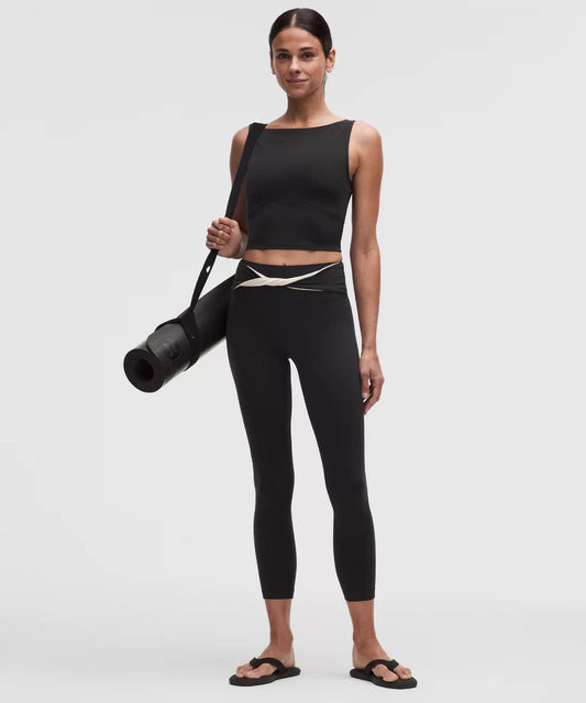 Woman in black athletic wear holding a yoga mat on a white background