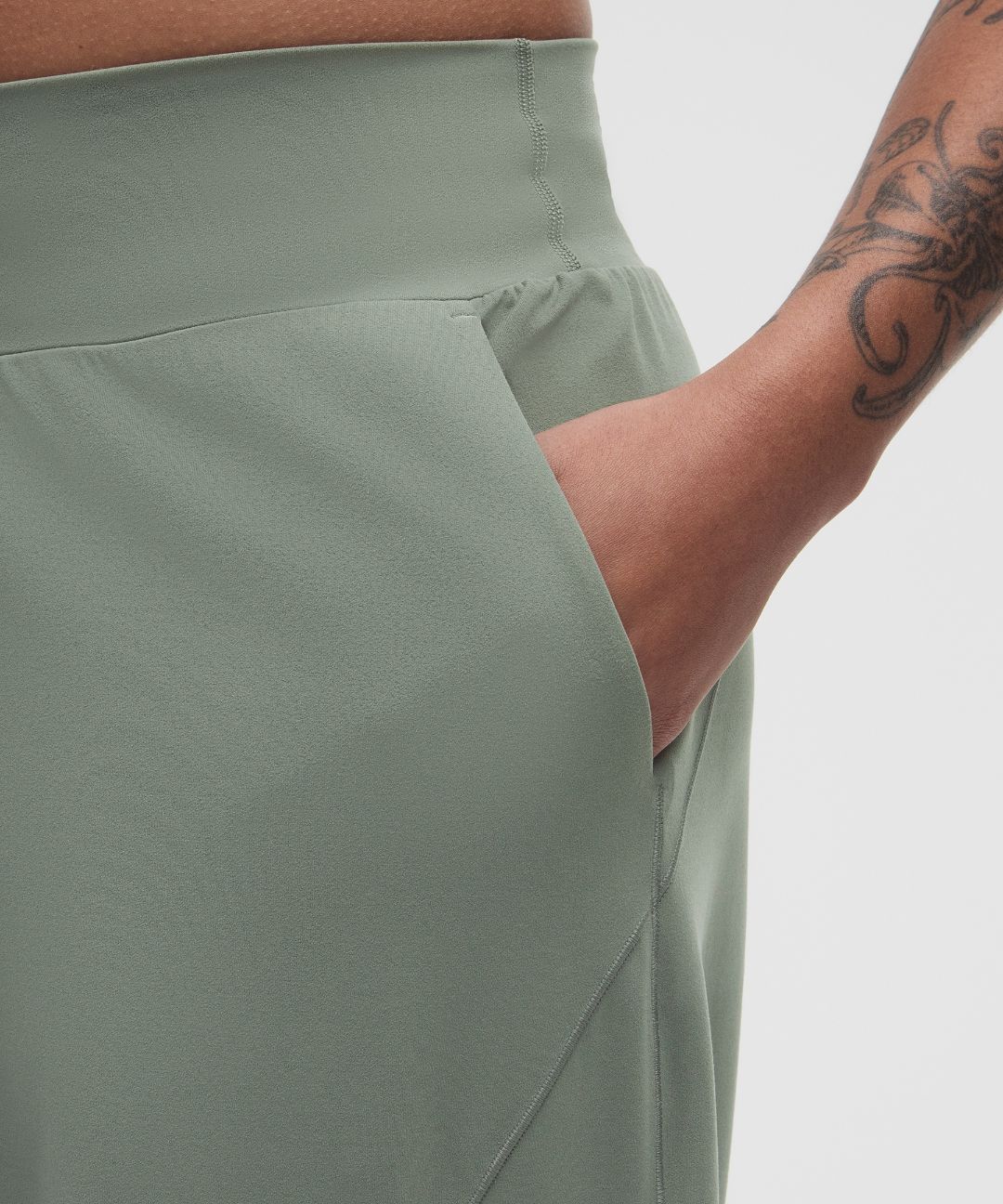 Person wearing light green pants with a tattooed arm on a plain background