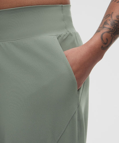 Person wearing light green pants with a tattooed arm on a plain background