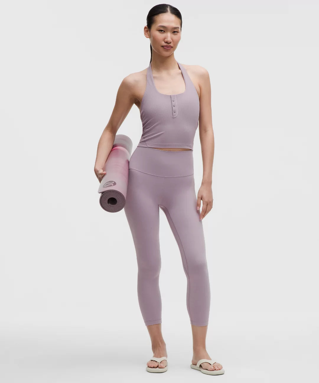 Woman in lavender athletic wear holding a yoga mat on a white background