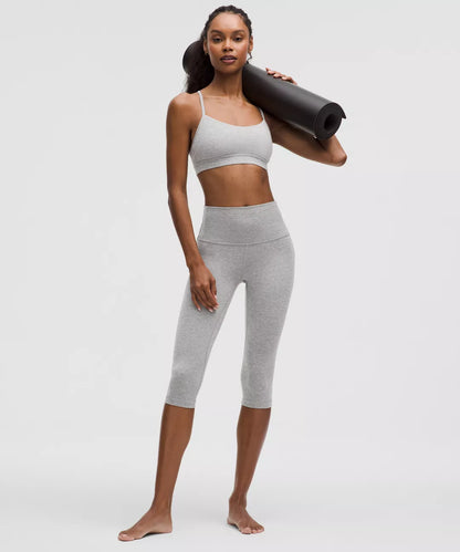 Woman in gray athletic wear holding a yoga mat on a white background