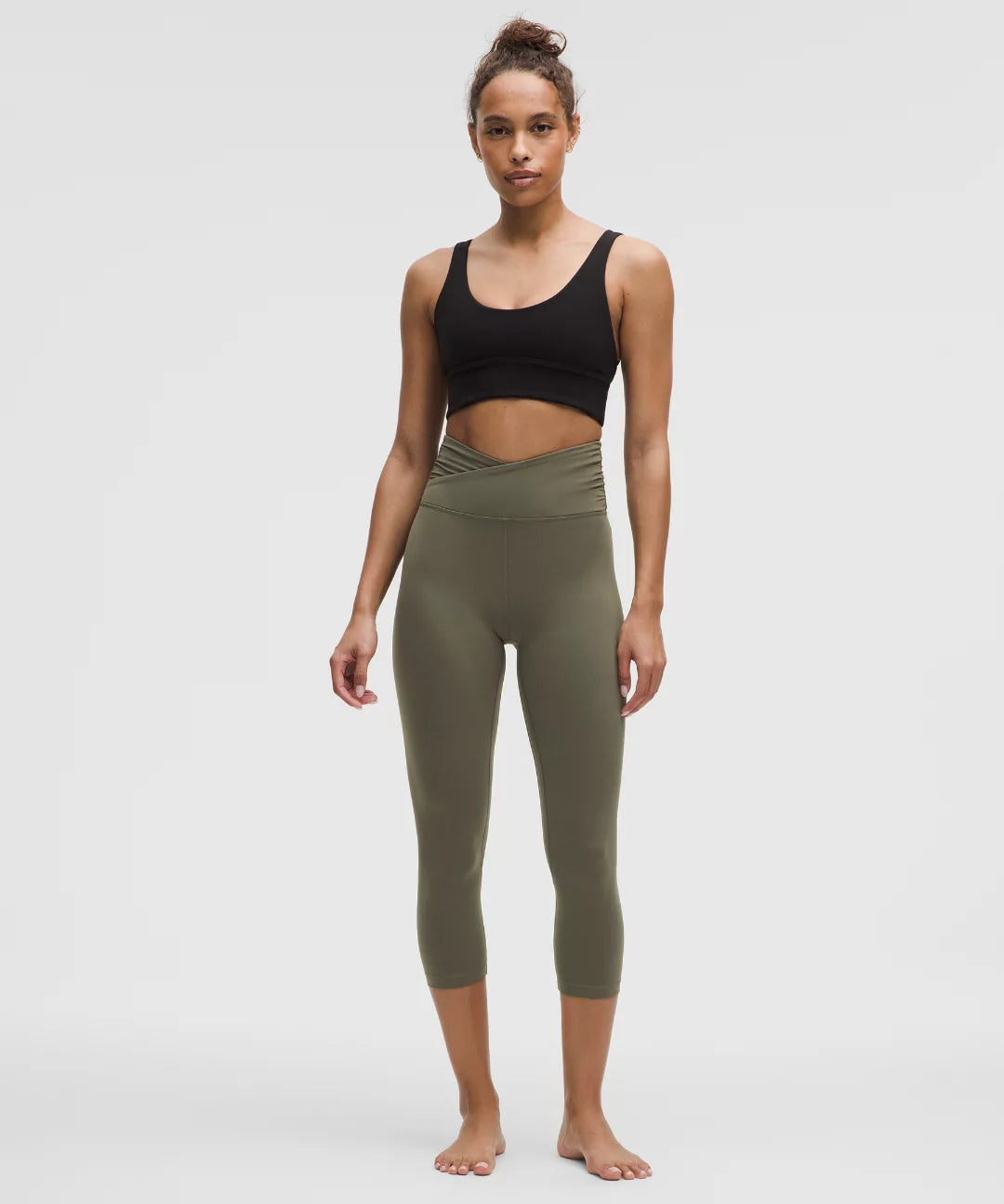 Woman wearing a black sports bra and olive green leggings on a white background