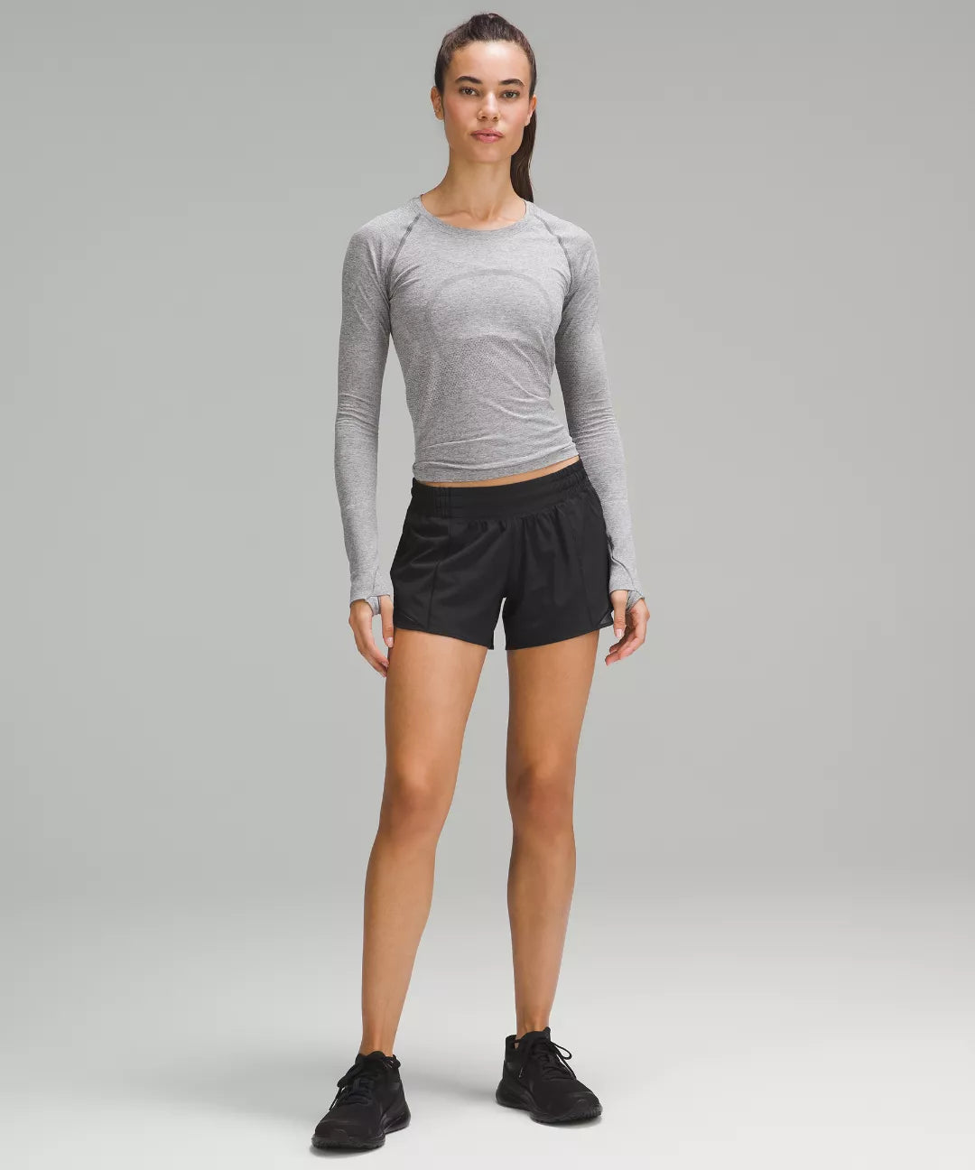 Woman wearing a gray long-sleeve top and black shorts on a gray background