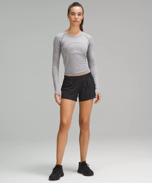 Woman wearing a gray long-sleeve top and black shorts on a gray background