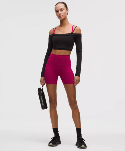 Person wearing a black long-sleeve crop top and pink shorts, holding a water bottle on a white background