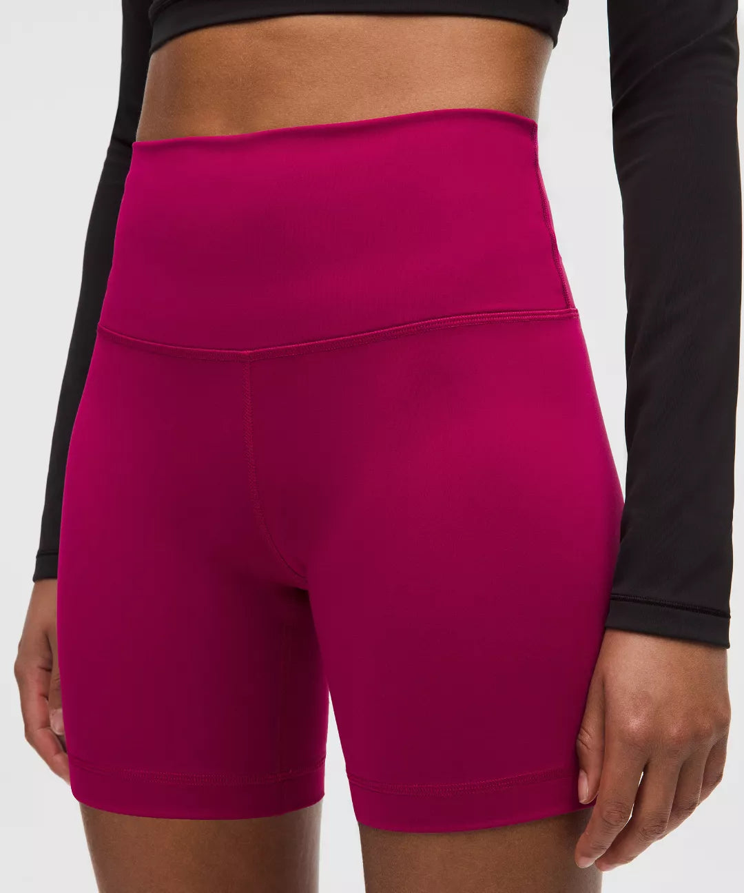 Person wearing bright pink athletic shorts with a black long-sleeve top on a white background