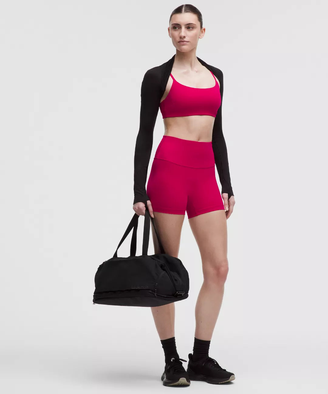 Woman in pink athletic outfit holding a black duffel bag on a white background