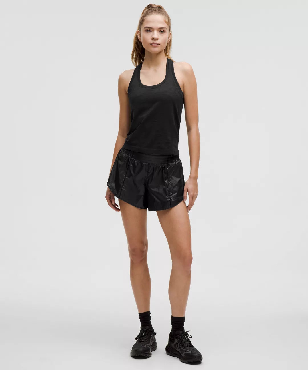 Woman wearing a black tank top and shorts on a white background