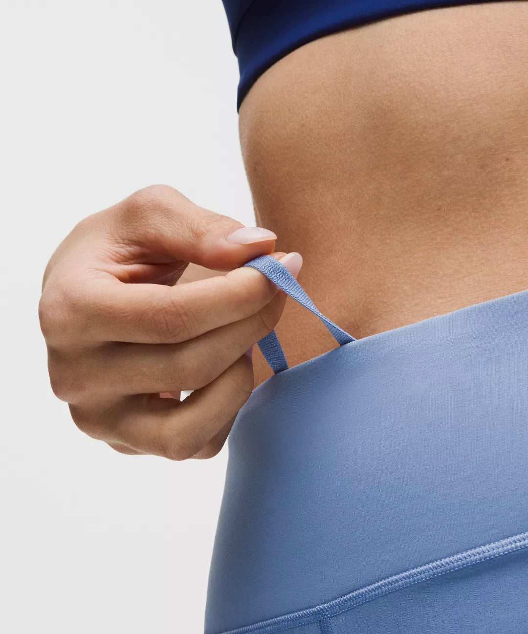 Person adjusting a blue sports bra strap against a neutral background