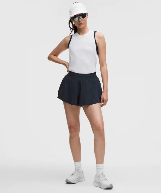 Woman wearing a white tank top, black shorts, and white sneakers on a white background