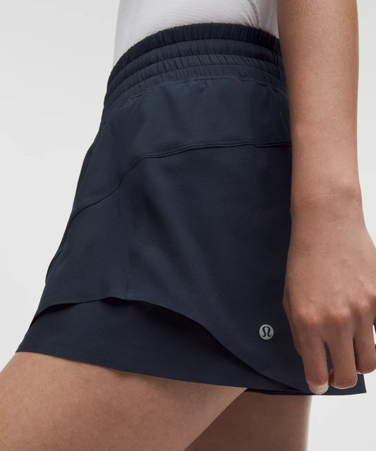 Person wearing navy blue athletic shorts with a visible brand logo on a light gray background