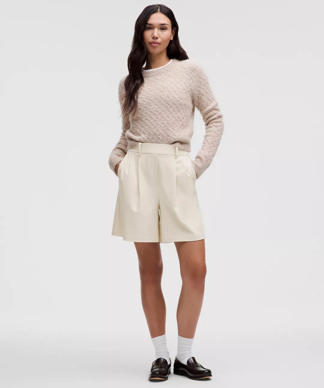 Woman wearing a beige sweater and cream shorts on a white background