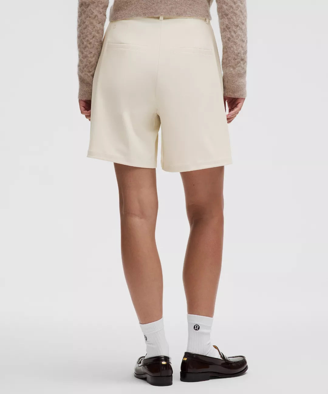 Person wearing a beige skirt, brown sweater, white socks, and black shoes on a white background