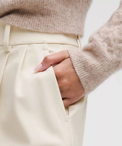 Close-up of a person wearing a beige sweater and cream pants with a neutral background