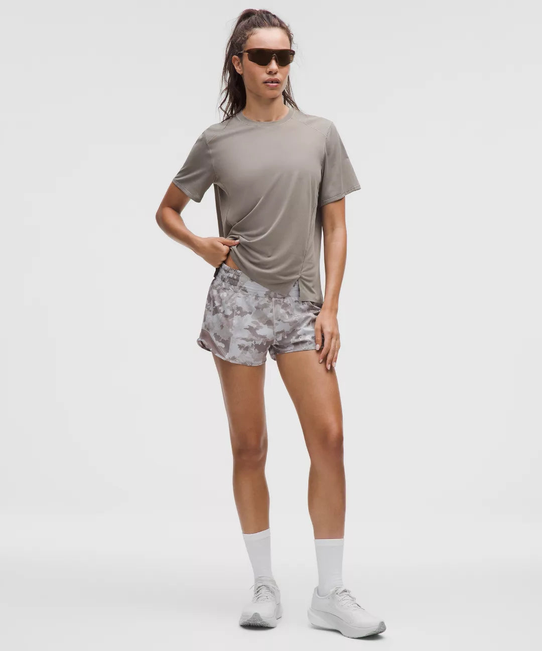 Woman wearing a gray t-shirt, patterned shorts, and white sneakers on a white background