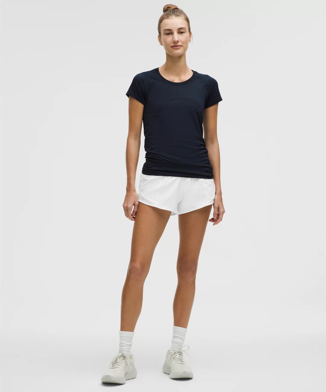 Woman wearing a black t-shirt and white shorts on a plain background