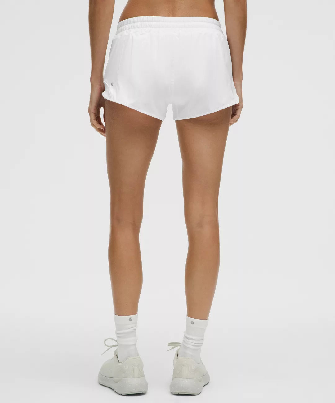 Person wearing white shorts and white sneakers on a plain background