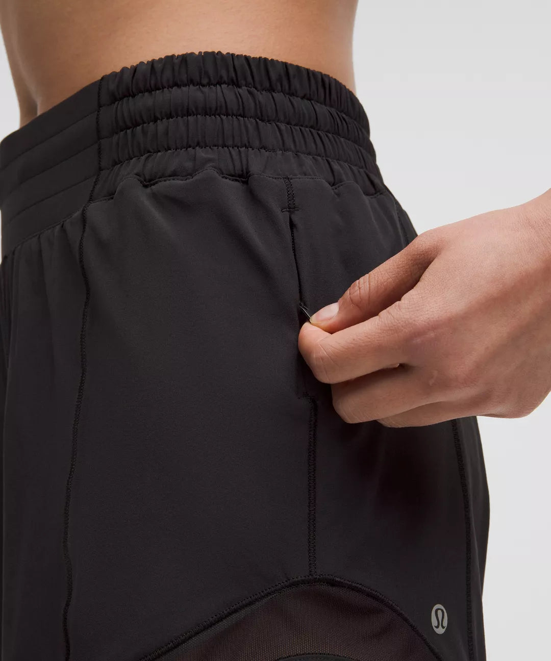 Person adjusting a black athletic shorts with a brand logo on a light gray background