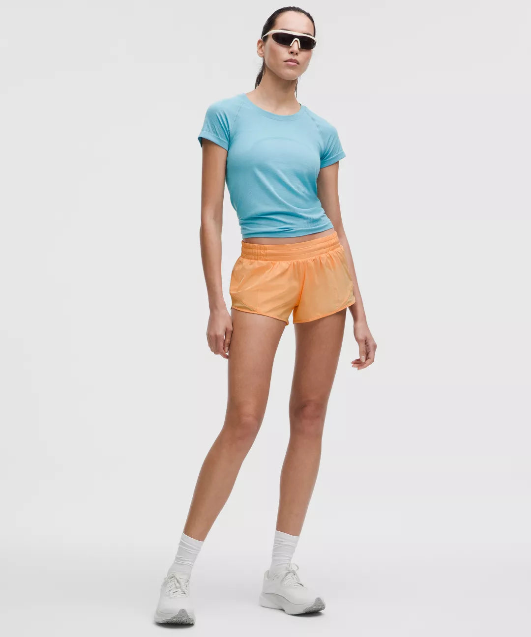 Person wearing a light blue t-shirt and orange shorts on a white background