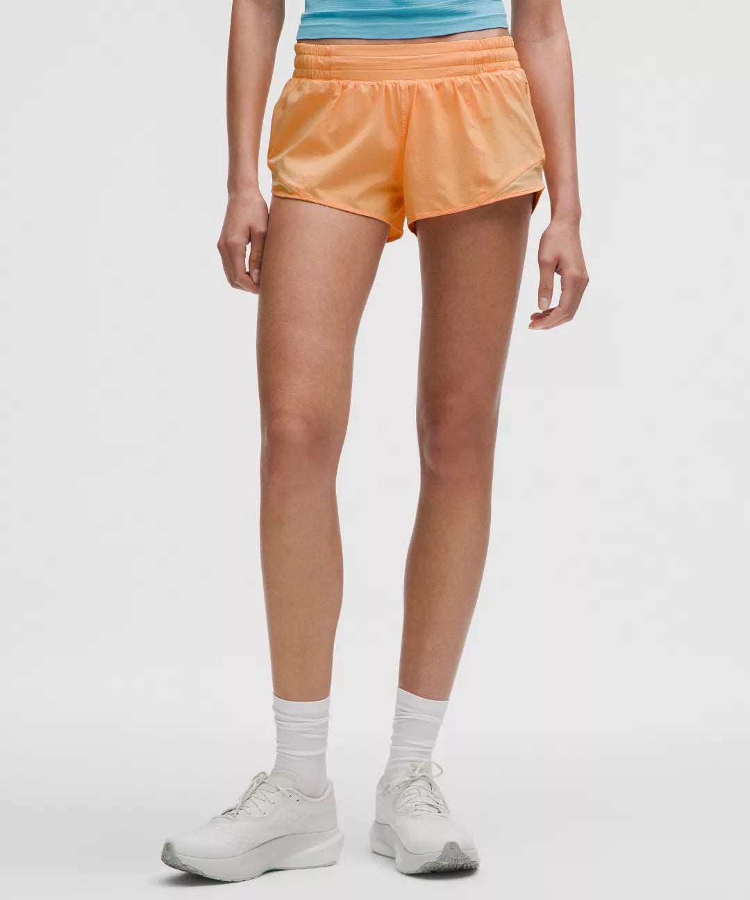 Person wearing orange shorts and white sneakers on a plain background