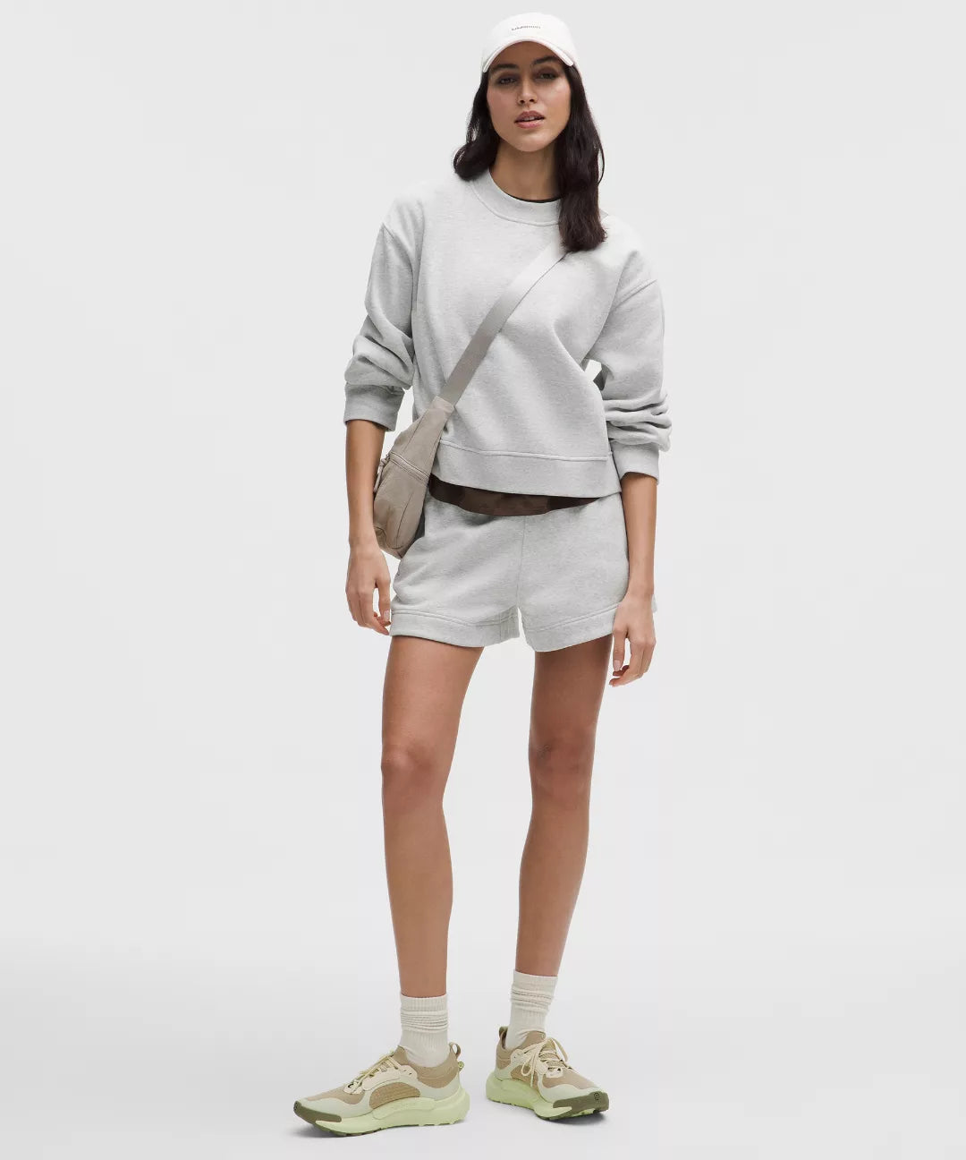 Person wearing a light gray sweatshirt, shorts, and sneakers on a white background