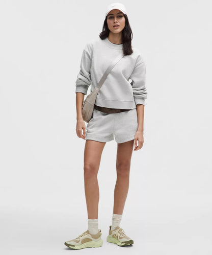 Person wearing a light gray sweatshirt, shorts, and sneakers on a white background