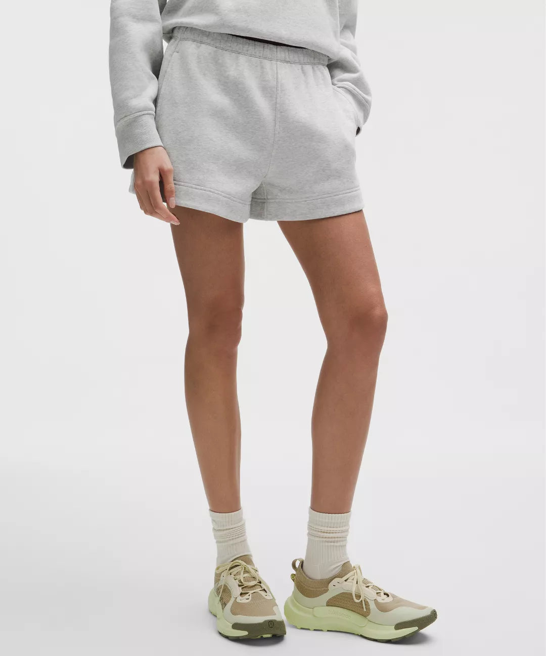 Person wearing gray sweatshirt and shorts with beige sneakers on a white background