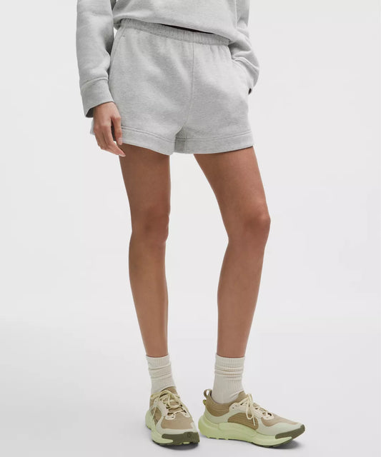 Person wearing gray sweatshirt and shorts with beige sneakers on a white background