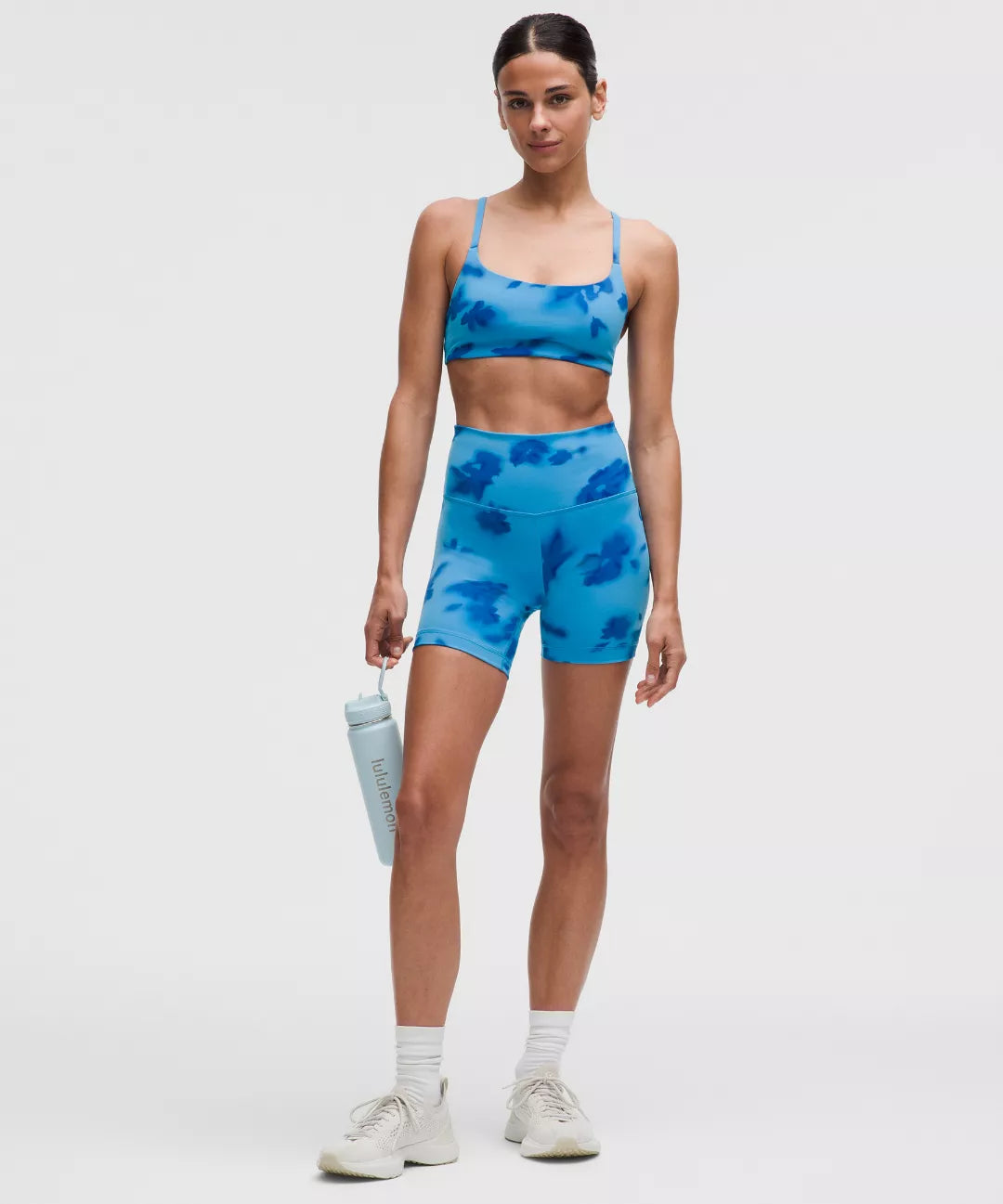 Woman wearing a blue athletic outfit with a sports bra and shorts, holding a water bottle.