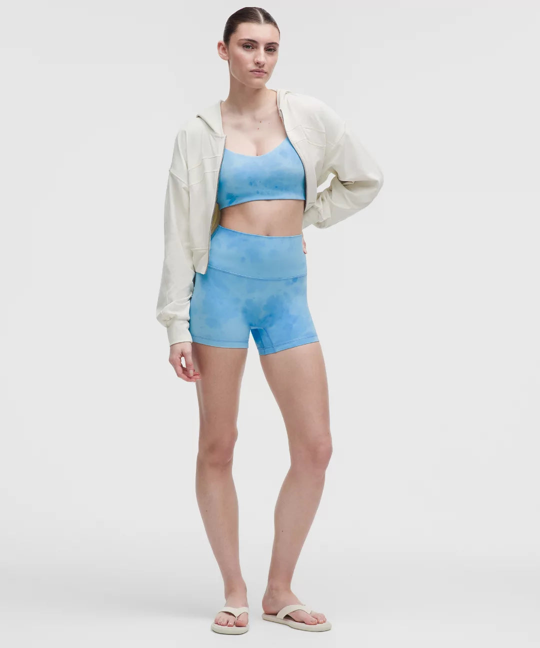 Woman wearing a light blue athletic outfit with a white jacket on a plain background